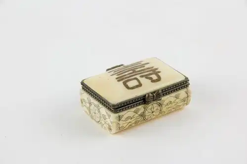 Kleine Dose,
Tibet, 20. Jh., Bein, Deckel mit Schriftzeichen verziert, Korpus graviert und geschwärzt, Gebrauchsspuren. 
L: 4,5 cm, B: 3 cm
Little box with cover, bone, Tibet, 20th century, decorated, good condition