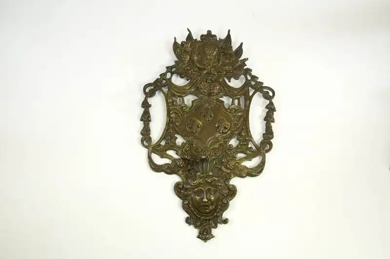 Wandapplikation, Frankreich, 17./18. Jh., Bronze, in der Mitte das französische Wappen, bekrönt von 2 Putten, und dem Portrait von Ludwig dem XIV, flankiert von Wappen und Kriegsgirlanden, im Unterteil Frauenkopf, Leuchterarm fehlt, Rest einer... 0