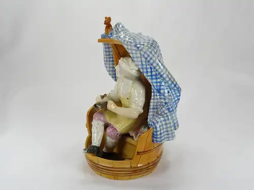 Porzellanfigur, 18./19. Jh., wohl England, Meißenkopiemarke, auf Glasur, in Fass sitzender Schuster bei der Reparatur eines Stiefels, polychrom bemalt, 2 große Brandrisse, 3 kleine Brandrisse im Fassboden, Gebrauchsspuren, sehr originell. H: 18 cm,...