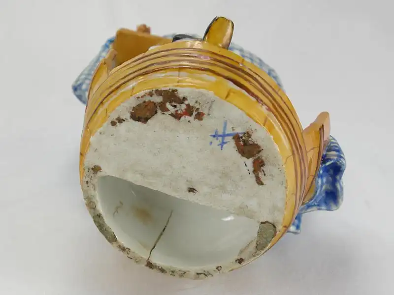 Porzellanfigur, 18./19. Jh., wohl England, Meißenkopiemarke, auf Glasur, in Fass sitzender Schuster bei der Reparatur eines Stiefels, polychrom bemalt, 2 große Brandrisse, 3 kleine Brandrisse im Fassboden, Gebrauchsspuren, sehr originell. H: 18 cm,... 6