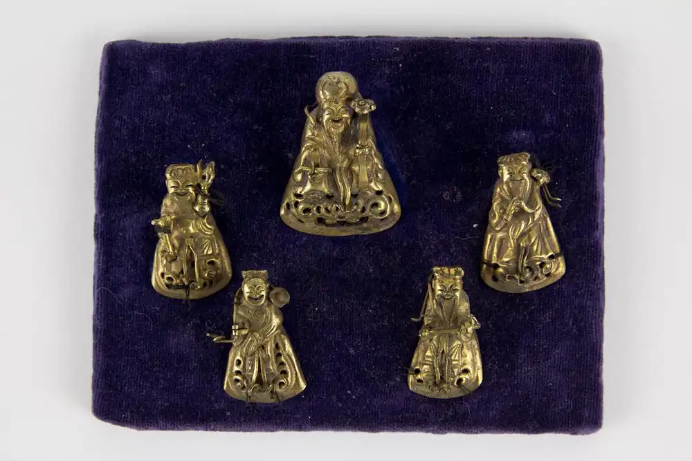 Glücksgötter, China, um 1900, Glücksgötter für Mützen, wohl Silber, vergoldet, auf Samtkissen genäht, Gebrauchsspuren. H: 3,5 cm bis 4 cm 0