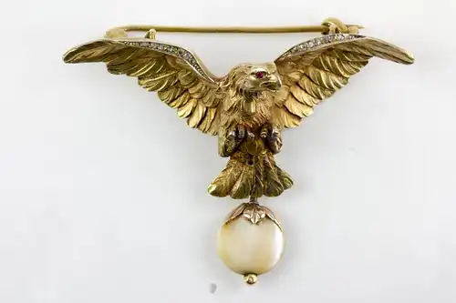 Brosche, um 1900, in Form eines Adlers, Silber vergoldet, Augen mit kleinen Rubinen besetzt, Flügelkanten mit Rosendiamanten, anhängend eine Perlmutscheibe in Rotgold gefasst, sehr feine Ausführung. H: 4 cm, B: 5,7 cm