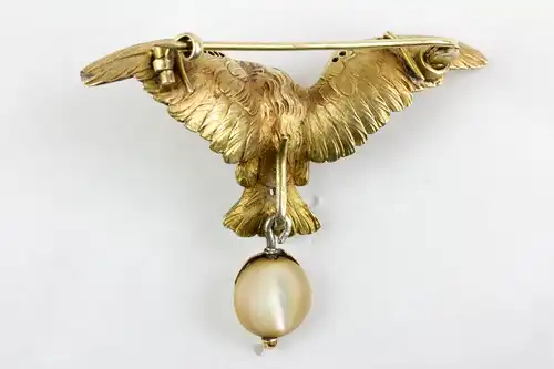 Brosche, um 1900, in Form eines Adlers, Silber vergoldet, Augen mit kleinen Rubinen besetzt, Flügelkanten mit Rosendiamanten, anhängend eine Perlmutscheibe in Rotgold gefasst, sehr feine Ausführung. H: 4 cm, B: 5,7 cm