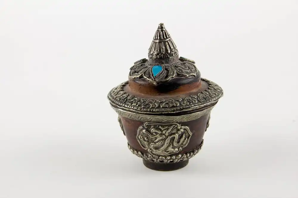 Teeschale, mit Deckel und Ständer, Tibet, 20. Jh., gedrechselte Holzkörper, reichlich mit Weißmetall und Türkisen verziert, Gebrauchsspuren. 

Teapot with cover, Tibet, 20th century, wood, decorated with metal and Turkey stone. 0