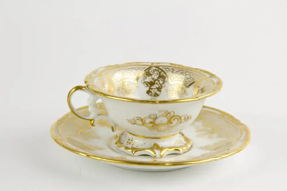 Tasse und Untertasse, Schlesien, Mitte 19. Jh., Gold- und Blumenmalerei, auf Tassengrund Darstellung eines pfeiferauchenden Puttos auf Wolke. H: 6 cm. 1