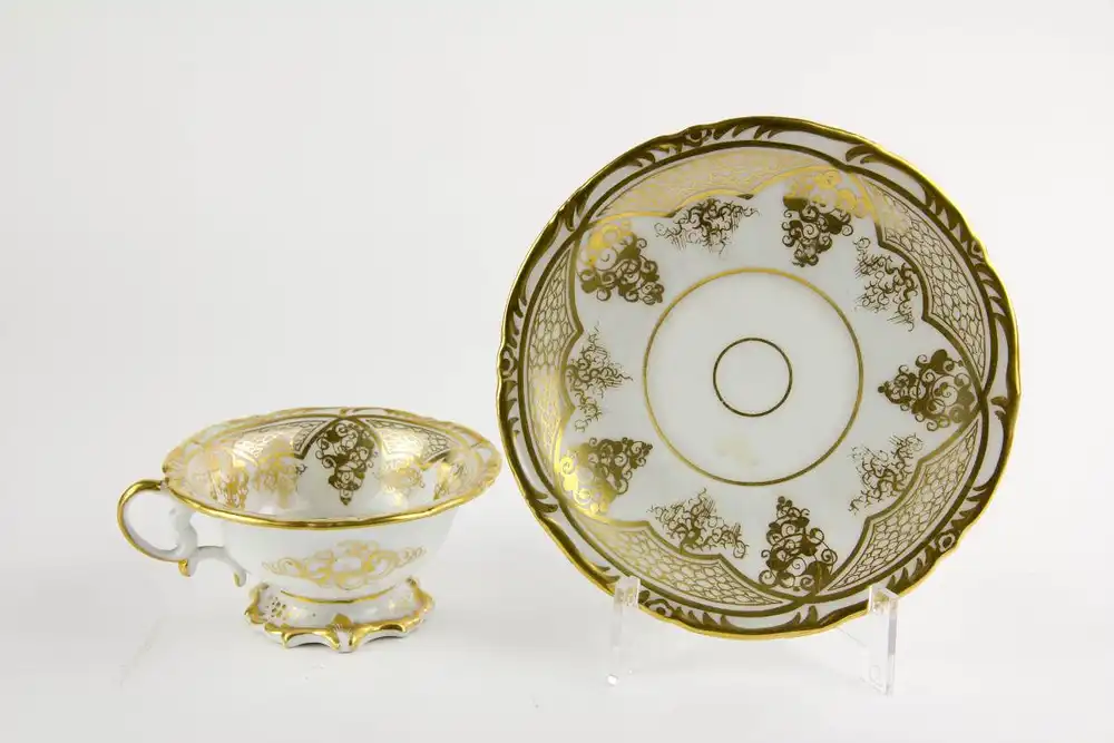 Tasse und Untertasse, Schlesien, Mitte 19. Jh., Gold- und Blumenmalerei, auf Tassengrund Darstellung eines pfeiferauchenden Puttos auf Wolke. H: 6 cm. 2