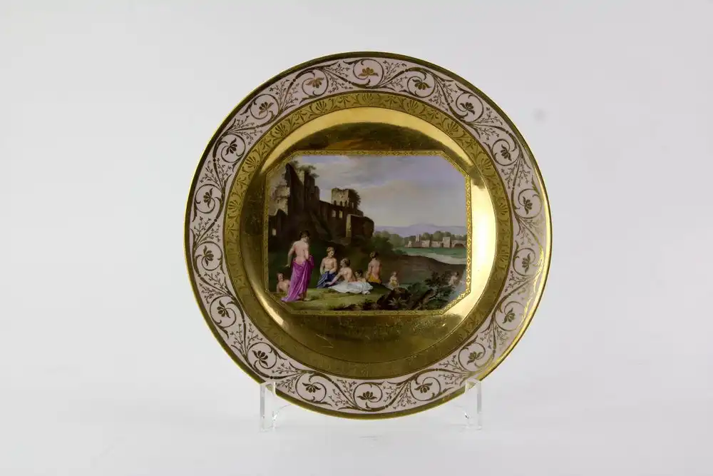 Teller, um 1800, gemarkt KPM Berlin, im Fond Kartusche mit italienischer Landschaft, Ruinen und Personenstaffage, reich vergoldet und radiert, Fahne zartrosa mit Goldornamenten, unbeschädigt, minimal berieben. D: 24,5 cm.  Plate, about 1800, marked... 0