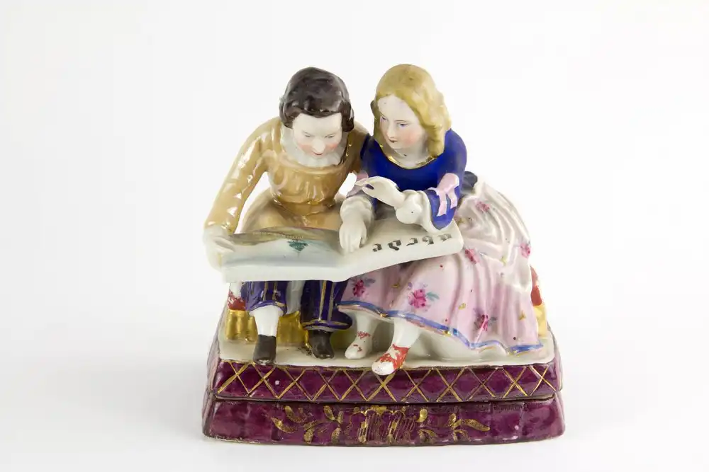 Schreibtischgarnitur, Thüringen, Mitte 19. Jh., ungemarkt, polychrom bemalt, in Form von 2 sitzenden Kindern, ein Schulbuch lesend, im inneren 2 Gefäße mit Masken aufgelegt für Tinte und Sand, stärkerer Farbabrieb, Gebrauchsspuren. H: 15 cm, B:... 0