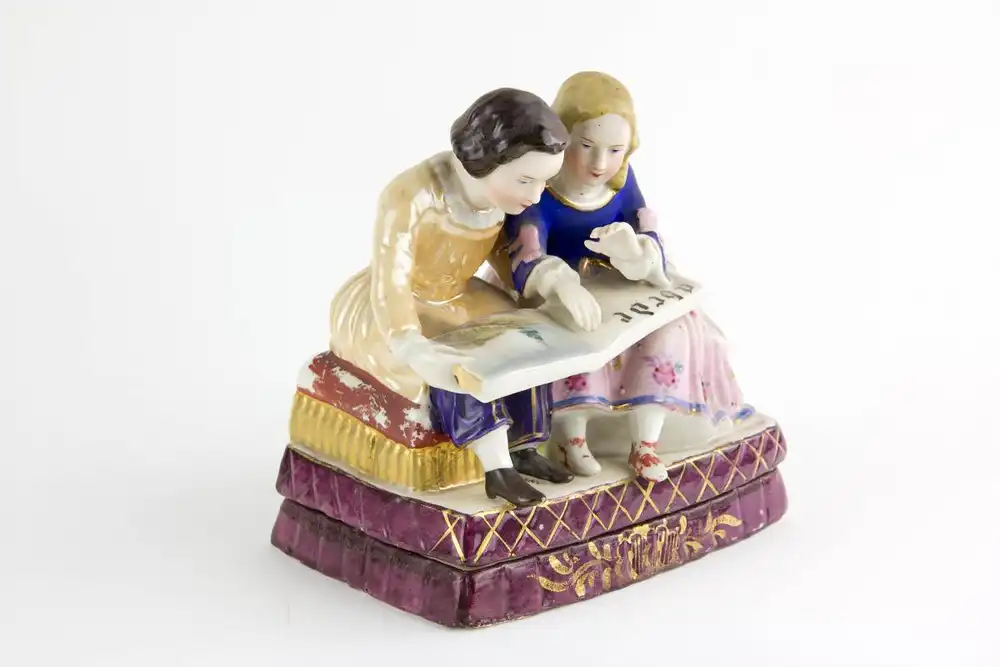 Schreibtischgarnitur, Thüringen, Mitte 19. Jh., ungemarkt, polychrom bemalt, in Form von 2 sitzenden Kindern, ein Schulbuch lesend, im inneren 2 Gefäße mit Masken aufgelegt für Tinte und Sand, stärkerer Farbabrieb, Gebrauchsspuren. H: 15 cm, B:... 1