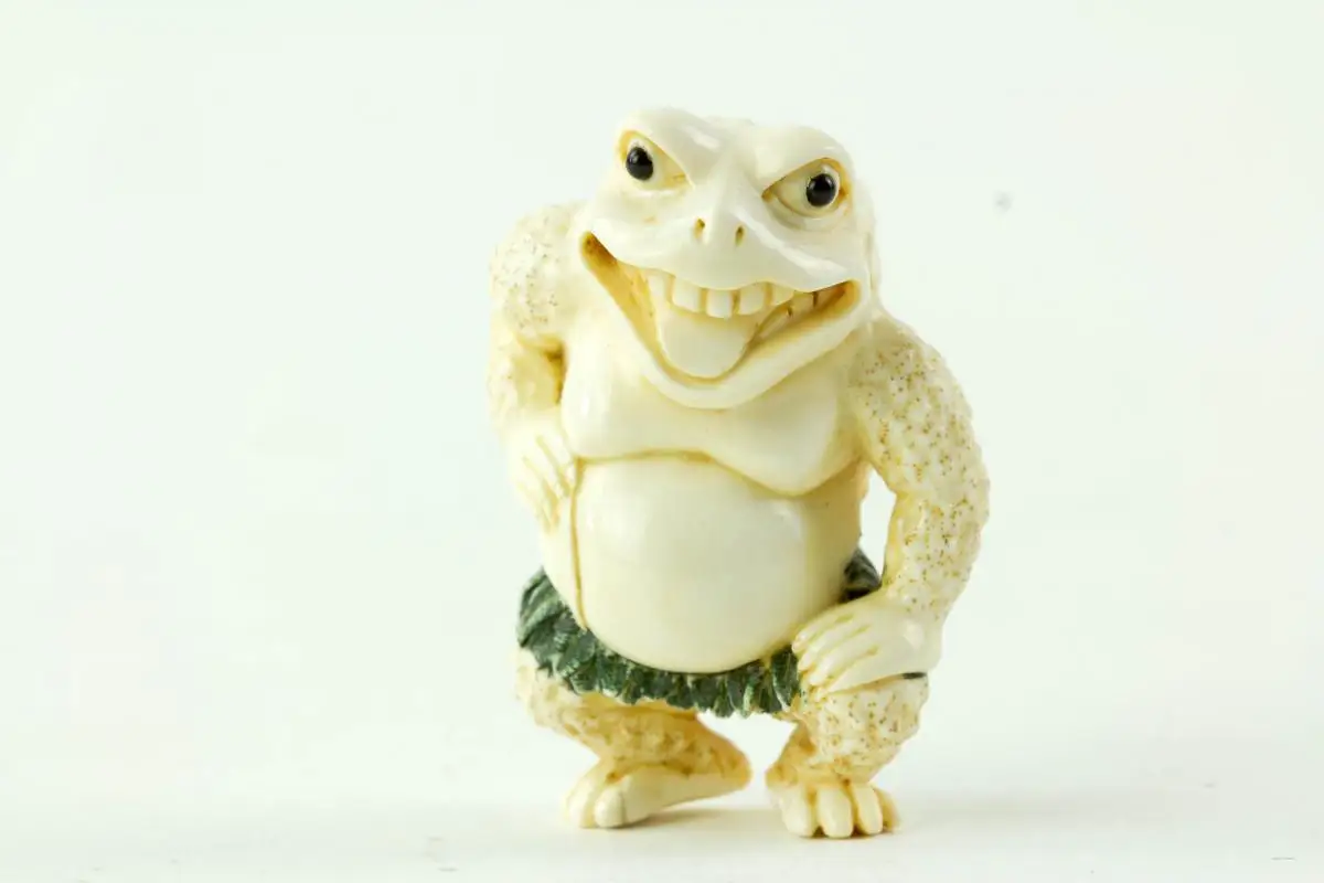 Netsuke, Japan, Taisho-Zeit, Elfenbein, signiert, humoristische Darstellung einer Kröte mit grün gefasstem Blätterrock, sehr feine Ausarbeitung, H: 4,5 cm. 0