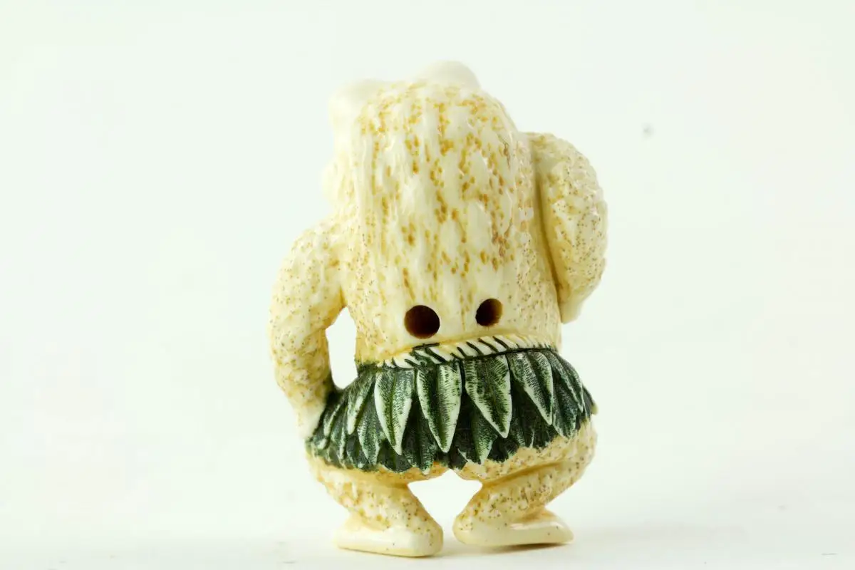 Netsuke, Japan, Taisho-Zeit, Elfenbein, signiert, humoristische Darstellung einer Kröte mit grün gefasstem Blätterrock, sehr feine Ausarbeitung, H: 4,5 cm. 2