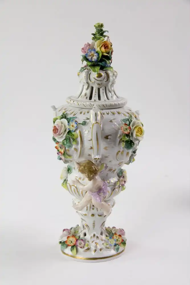 Kleine Duftvase, Mitte 20. Jh., Bindeschild Marke Thüringen, reichlich goldverziertes Gefäß mit Henkeln und Deckeln, mit plastisch aufgelegten Blüten und Puttis, stärker bestoßen, H: 29 cm. 1