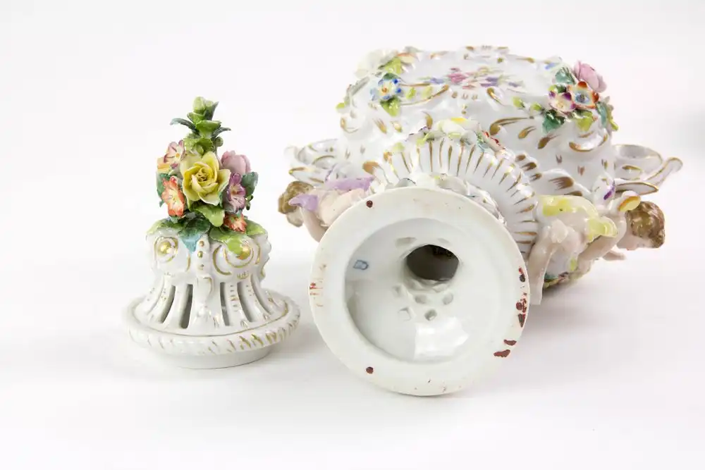 Kleine Duftvase, Mitte 20. Jh., Bindeschild Marke Thüringen, reichlich goldverziertes Gefäß mit Henkeln und Deckeln, mit plastisch aufgelegten Blüten und Puttis, stärker bestoßen, H: 29 cm. 5