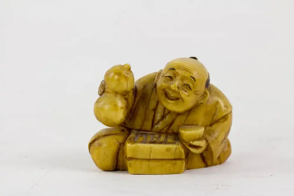 Netsuke, Japan, Meiji Zeit, um 1900, signiert, Elfenbein, sitzender Mann mit Flaschenkürbis und Schale, Gebrauchsspuren. H: 3,5 cm. 0