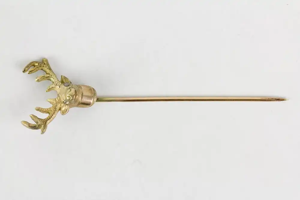 Krawattennadel, um 1900, 333er Gold, in Form eines Hirschkopfes, Augen mit Diamantsplittern belegt, eine Geweihstange leicht verbogen, Gebrauchsspuren. L:  6,9 cm, 3,2 g. 1