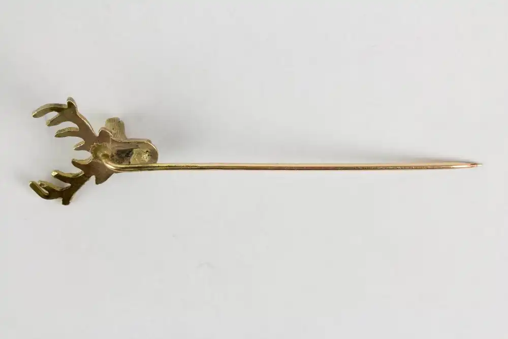 Krawattennadel, um 1900, 333er Gold, in Form eines Hirschkopfes, Augen mit Diamantsplittern belegt, eine Geweihstange leicht verbogen, Gebrauchsspuren. L:  6,9 cm, 3,2 g. 2
