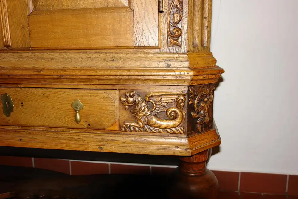 Stollenschrank, Barock, 2. Hälfte 18. Jh., norddeutsch, Eiche massiv, Korpus auf gedrechselten Säulen mit geschwungener Kreuzverstrebung, zweitürig, darunter zentrales Schubfach, Schubfach flankiert von zwei geschnitzten, geflügelten Löwen, neben... 2