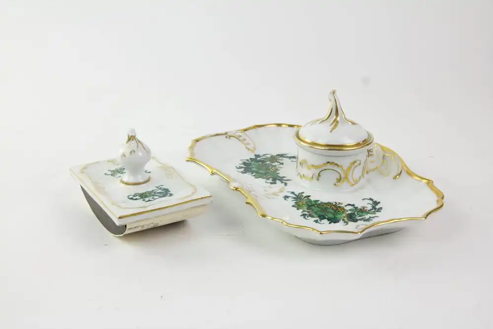 Schreibtischgarnitur, Anf.  Jh., gemarkt Fürstenberg, verziert mit grüner Blumenmalerei, goldverziert, Gold am Tablett etwas berieben, sonst guter, unbeschädigter Zustand. Tablett: 23 x 16 cm, Tintenlöscher: 11 x 6,5 cm. 0