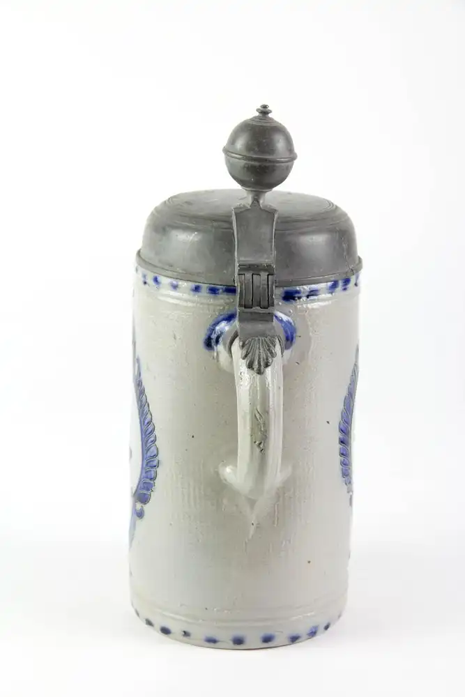 Krug, Westerwald, 19. Jh., mit Zinndeckel montiert, grauer Krug mit Blaumalerei in Ritzdekor, seitlicher Spannungsriss, sonst unbeschädigt. H: 25 cm. 1