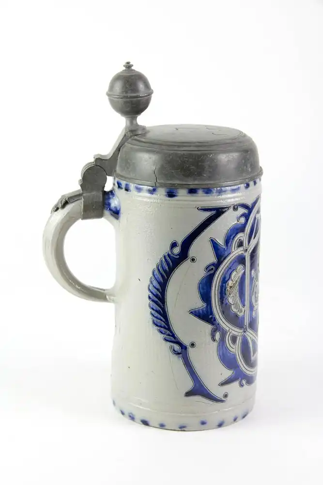 Krug, Westerwald, 19. Jh., mit Zinndeckel montiert, grauer Krug mit Blaumalerei in Ritzdekor, seitlicher Spannungsriss, sonst unbeschädigt. H: 25 cm. 3