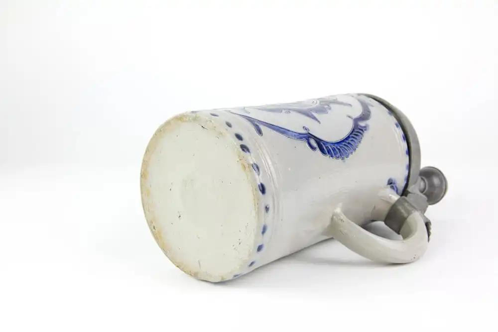 Krug, Westerwald, 19. Jh., mit Zinndeckel montiert, grauer Krug mit Blaumalerei in Ritzdekor, seitlicher Spannungsriss, sonst unbeschädigt. H: 25 cm. 4