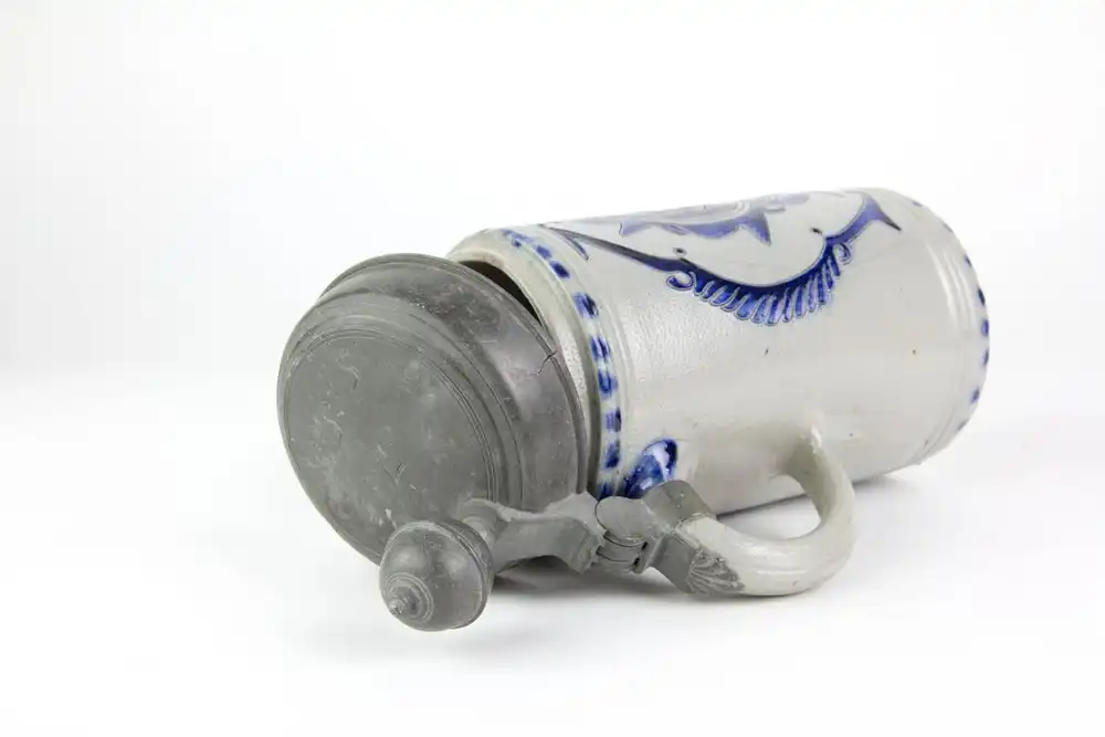 Krug, Westerwald, 19. Jh., mit Zinndeckel montiert, grauer Krug mit Blaumalerei in Ritzdekor, seitlicher Spannungsriss, sonst unbeschädigt. H: 25 cm. 5