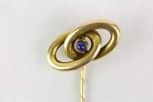 Krawattennadel, Anf. 20. Jh., gemarkt, 585er Gelbgold, zwei verschlungene Ringe, in der Mitte im Cabochon-Schliff gefasster Saphir, Gebrauchsspuren. L: 6,4 cm, 2,0 g.