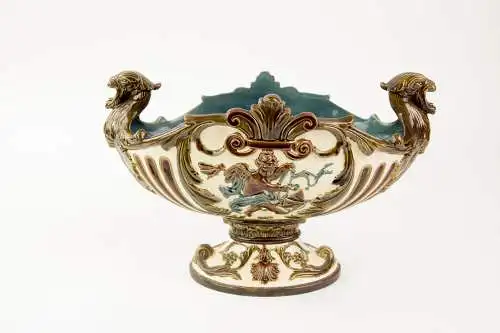 Prunkschale, um 1880, Historismus, Keramik, beigegrundig, erhaben verziert mit Ornamenten und beidseitig Putti unter Akanthusblatt, an den Seiten henkelförmiger Kopfabschluss, Gebrauchsspuren, L: 30 cm, H: 19 cm.