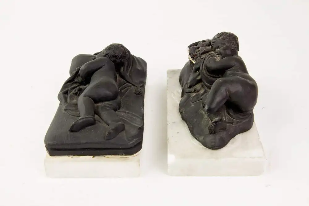 2 Figuren, 19. Jh., Wedgewood, Black Basalt, 2 schlafende Kinder, auf weißem Marmorsockel befestigt (geklebt), eine Figur mit stärkeren Beschädigungen und Restaurierungen, H: 6 cm, L: 14 cm. 4