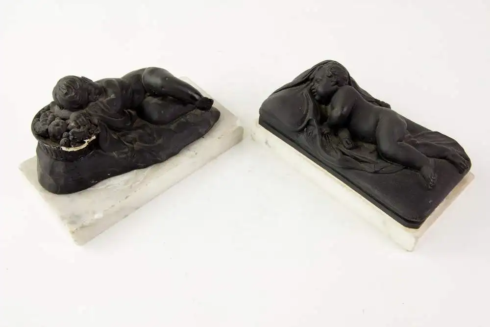 2 Figuren, 19. Jh., Wedgewood, Black Basalt, 2 schlafende Kinder, auf weißem Marmorsockel befestigt (geklebt), eine Figur mit stärkeren Beschädigungen und Restaurierungen, H: 6 cm, L: 14 cm. 9