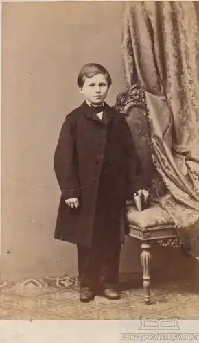 Portrait Junge in schwarzem Anzug mit Buch an Stuhl, Fotografie. Fotobild