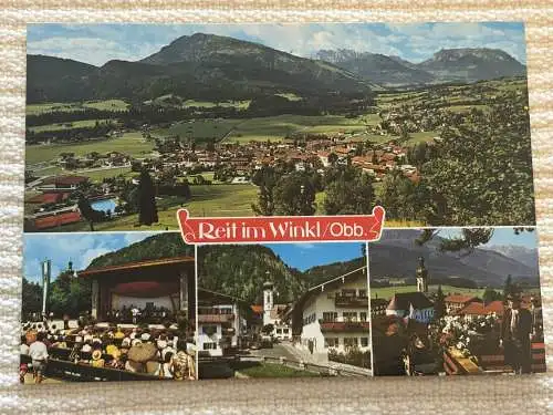 [Echtfotokarte farbig] Reit im Winkl / Obb. - Ortspanorama mit Kaisergebirgen und Unterberg,
Kurkonzert / Dorfstraße / Hochzeitslader. 