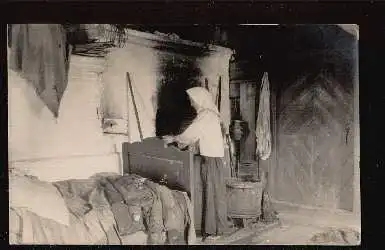 Innenansicht eines Bauernhauses mit einer Bäuerin am Ofen.