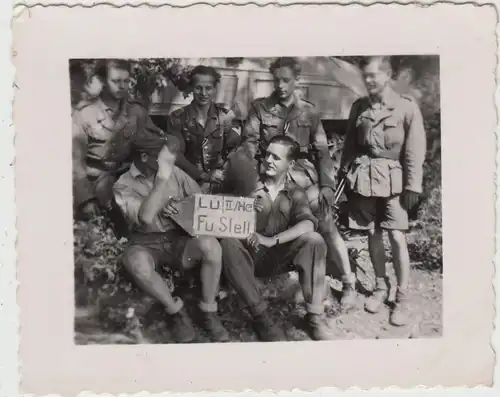 (F19945) Orig. Foto dt. Soldaten i. kurzen Hosen m. Schild >Lü.II/He Fu.Stelle