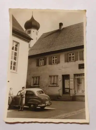 Frau vor Dorfladen mit Auto