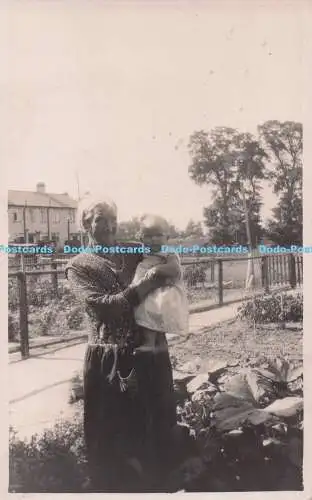 R693052 Alte Frau mit Baby im Arm steht in einem Garten