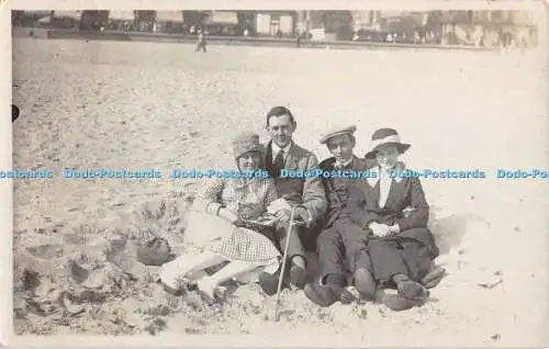 R417904 Zwei Frauen in dunklen Farben und Hut sitzen am Strand mit zwei Männern