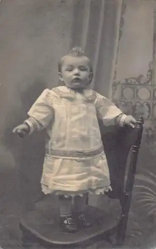 A696 Echt Foto Baby Mädchen im großen Kleid stehend auf Stuhl Vintage Postkarte