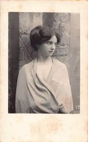 Frau mit Haaren im Dutt im Gewand posiert in Wandnähe Vintage Postkarte