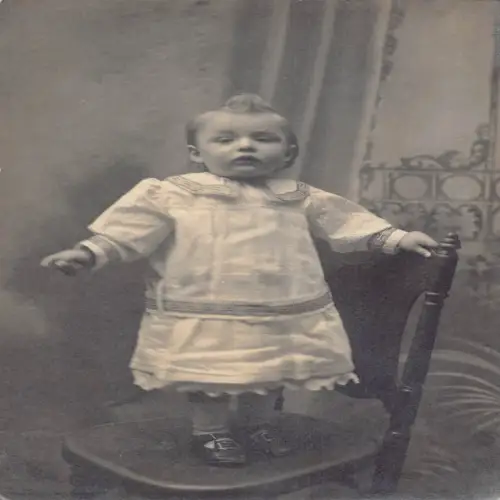 A696 Echt Foto Baby Mädchen im großen Kleid stehend auf Stuhl Vintage Postkarte