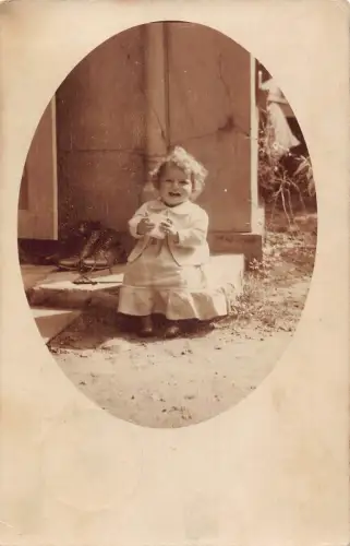 A631 Fröhliches Baby Mädchen im Kleid sitzt auf Veranda mit Becher Schuhe RPPC Postkarte