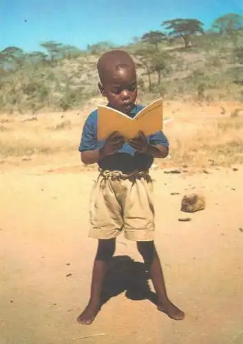 Postcard children types young African boy in desert reading a book