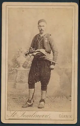 Fotografie St. Tomlinovic, Cernik, Portrait Mann in Tracht mit Pistolen & Dolch, rückseitig überstempelt Mostar