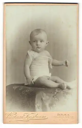 Fotografie Richard Kasbaum, Berlin N., Portrait eines Säuglings auf einem Polstermöbel