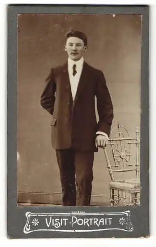Fotografie Fotograph u. Ort unbekannt, Portrait junger Mann im Anzug steht neben einem Stuhl