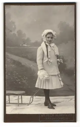Fotografie Wilhelm Klopp & Co., Braunschweig, Mädchen mit Zöpfen in modischer Winterkleidung zieht Schlitten
