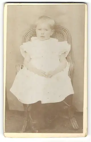 Fotografie niedliches Kind im weissen Kleid auf Stuhl sitzend