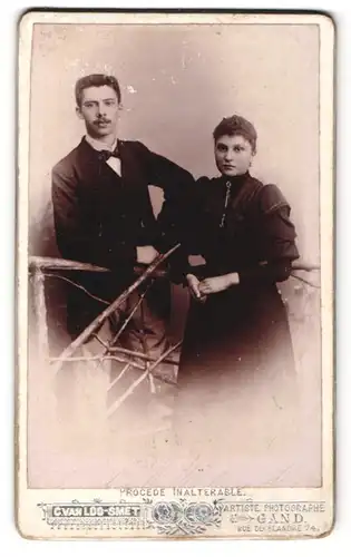 Fotografie G. van Loo-Smet, Gand, Paar steht am Zaun aus Ästen