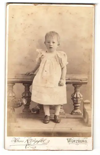 Fotografie Hans Klüpfel, Würzburg, niedliches kleines Mädchen im weissen Kleid lehnt am Geländer