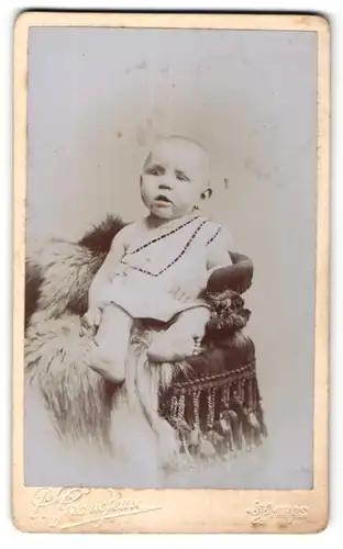 Fotografie P. Grandjean, Paris, niedliches Baby im weissen Kleid auf Felldecke sitzend
